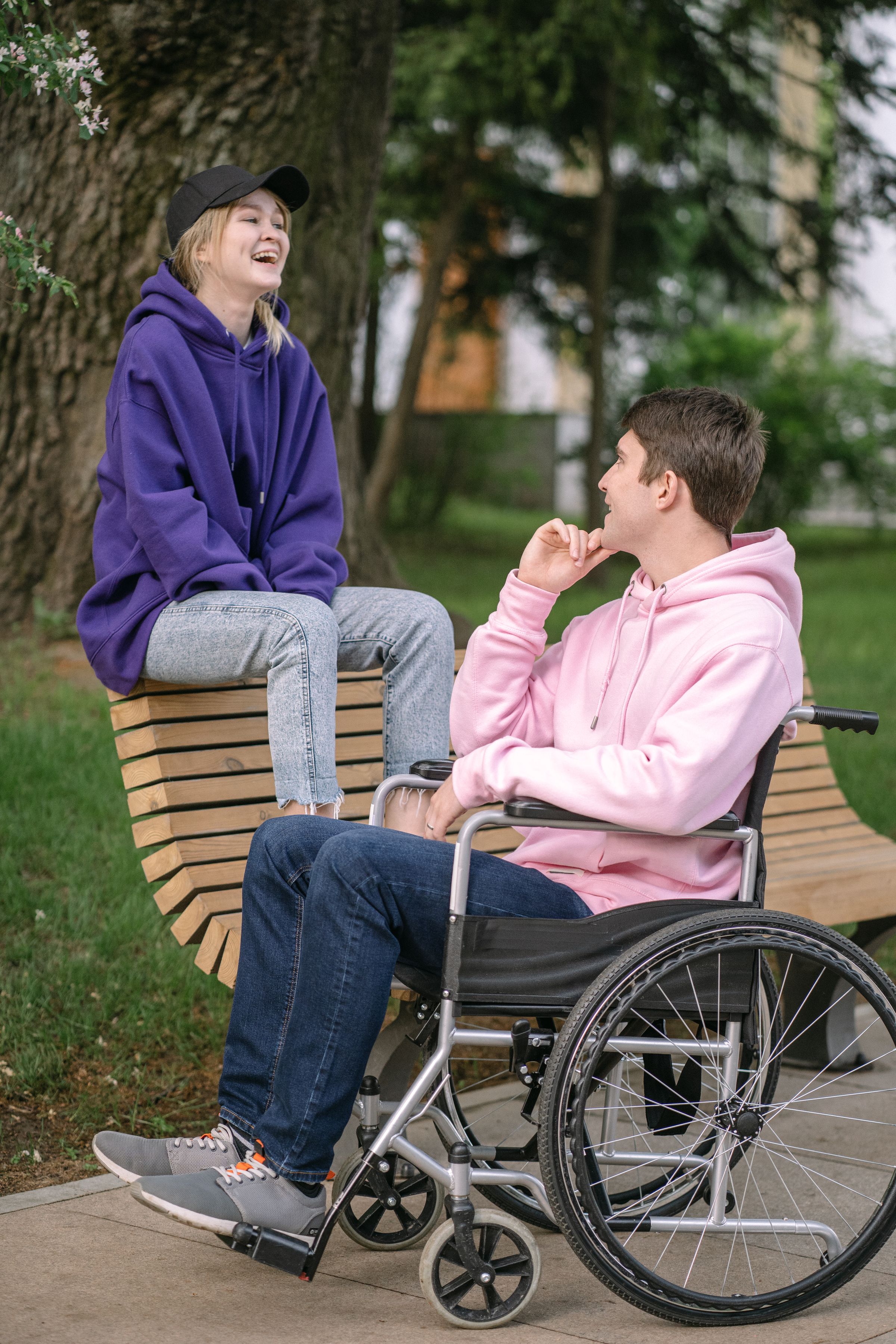 A wheelchair user and companion sharing a relaxed conversation in a park