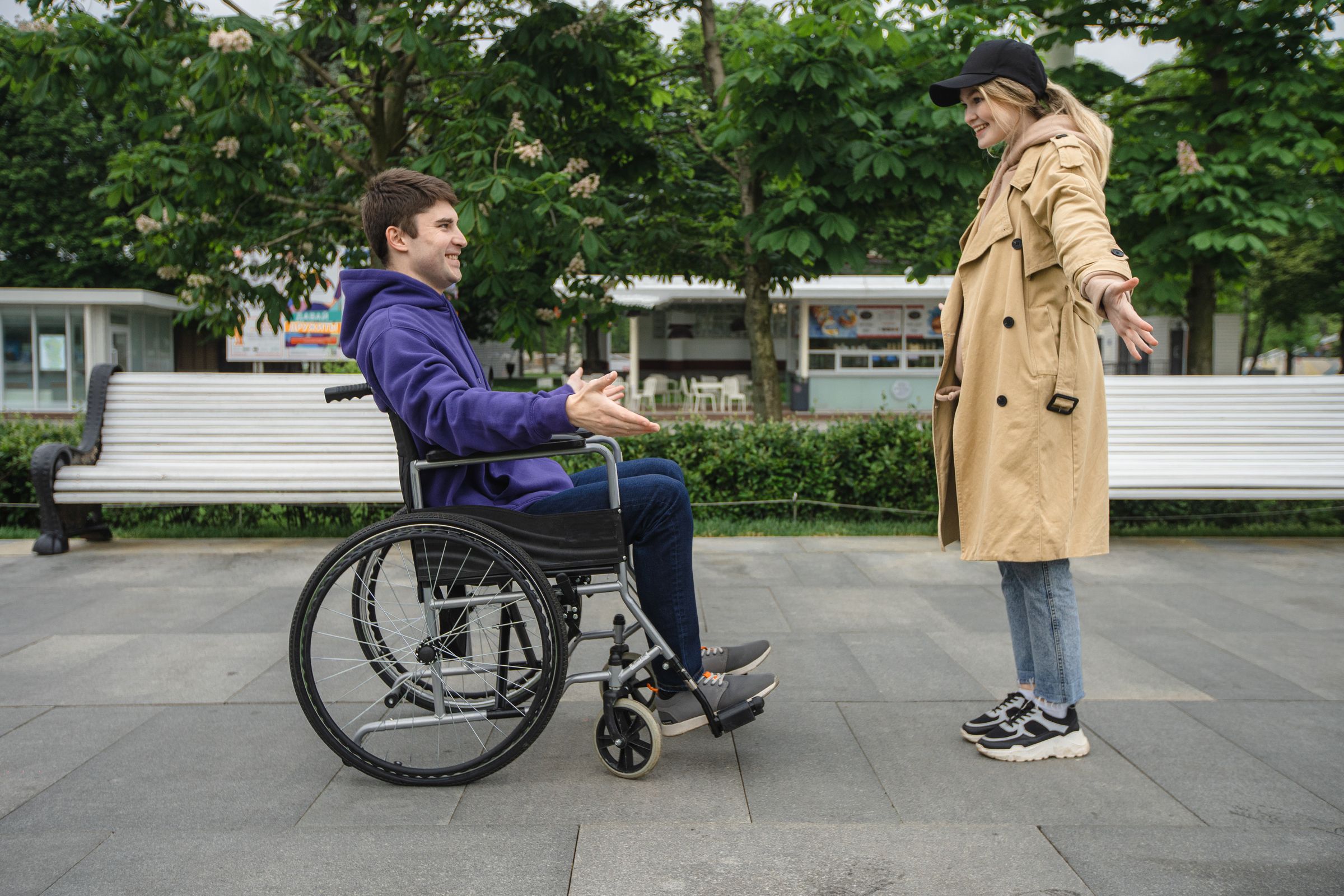 A wheelchair user greeting a friend in a leafy park