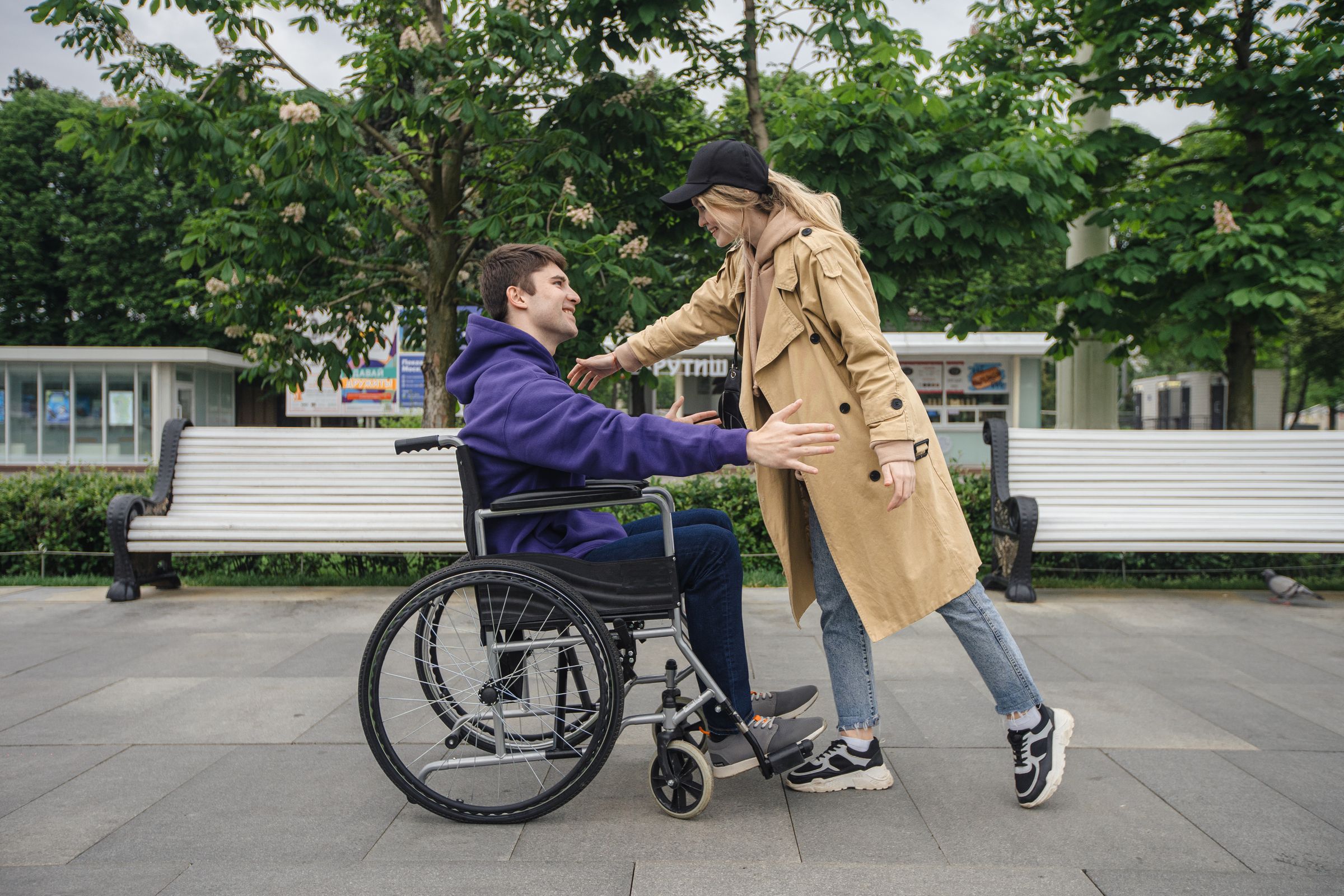 A wheelchair user greeting a companion in a leafy park